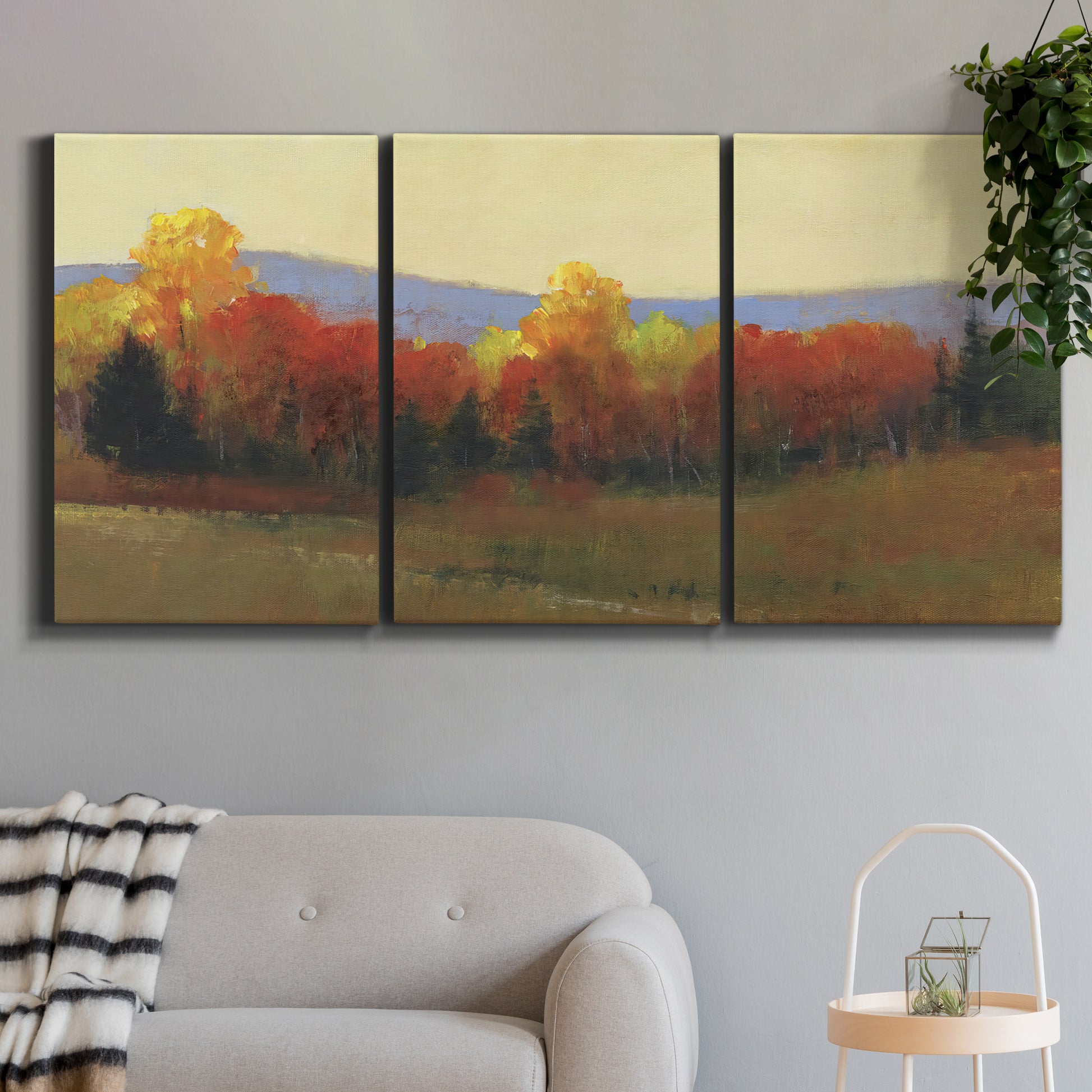 Three-panel canvas wall art featuring autumn landscape changing foliage, displayed in a modern living room above a sofa.