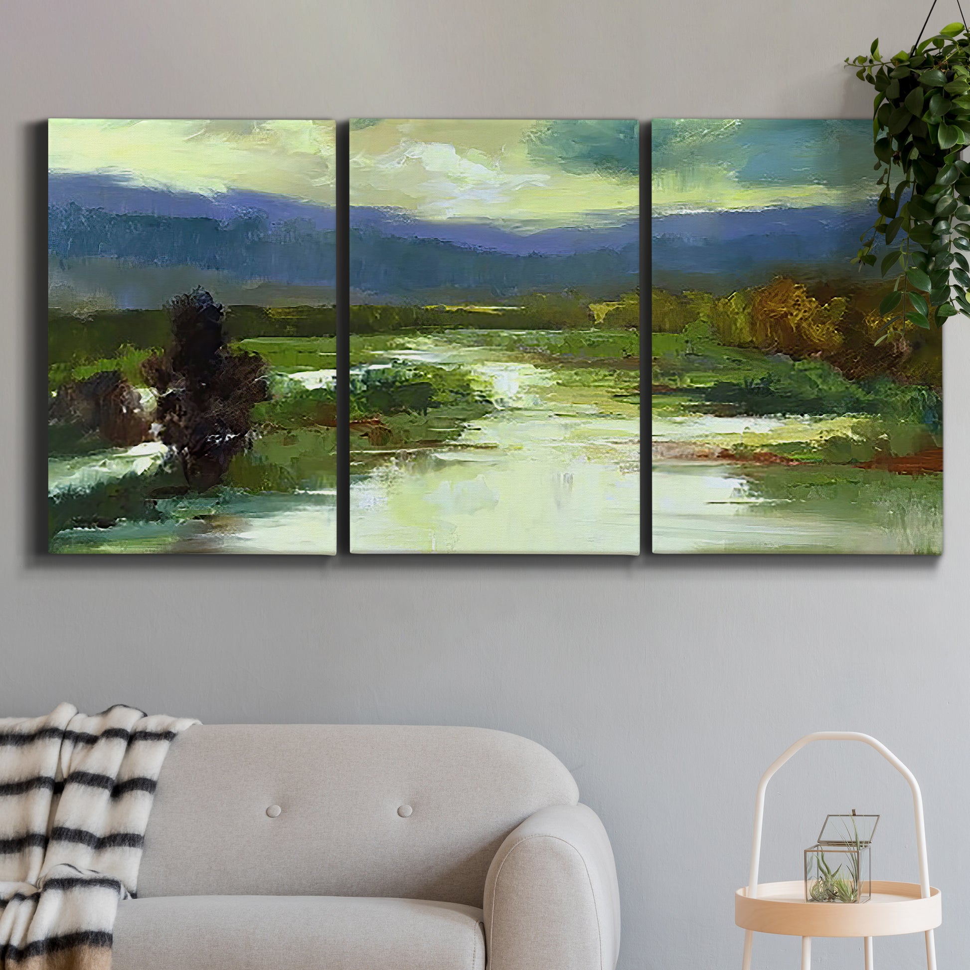 Three-panel canvas wall art featuring open meadow landscape with distant hills, displayed in a modern living room above a sofa.