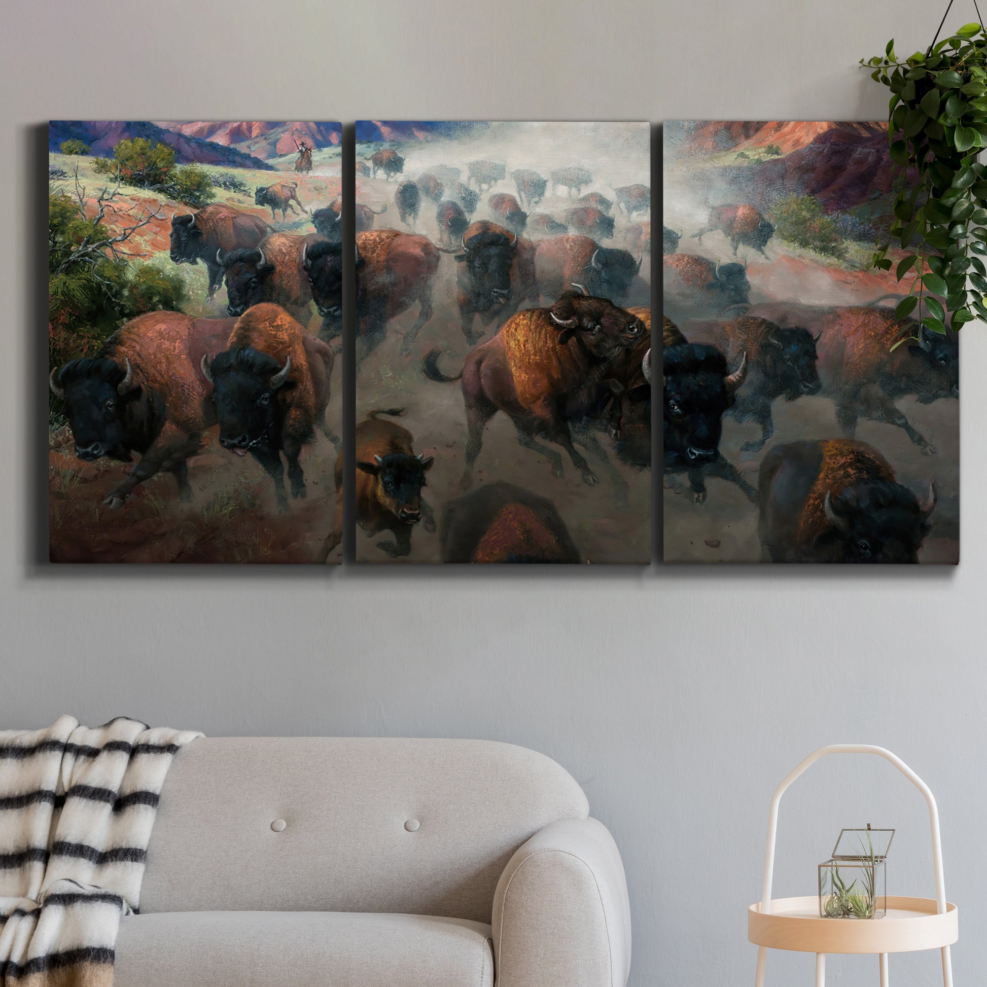 Three-panel canvas wall art featuring stormy canyon landscape with animals, displayed in a modern living room above a sofa.