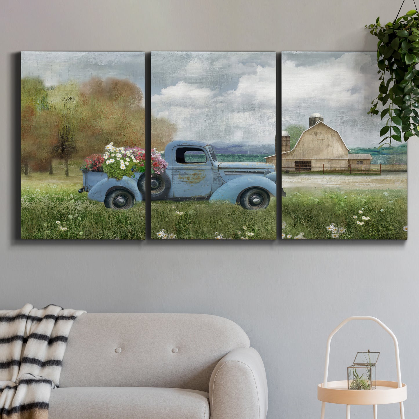 Three-panel canvas wall art featuring vintage blue truck with flower load, displayed in a modern living room above a sofa.