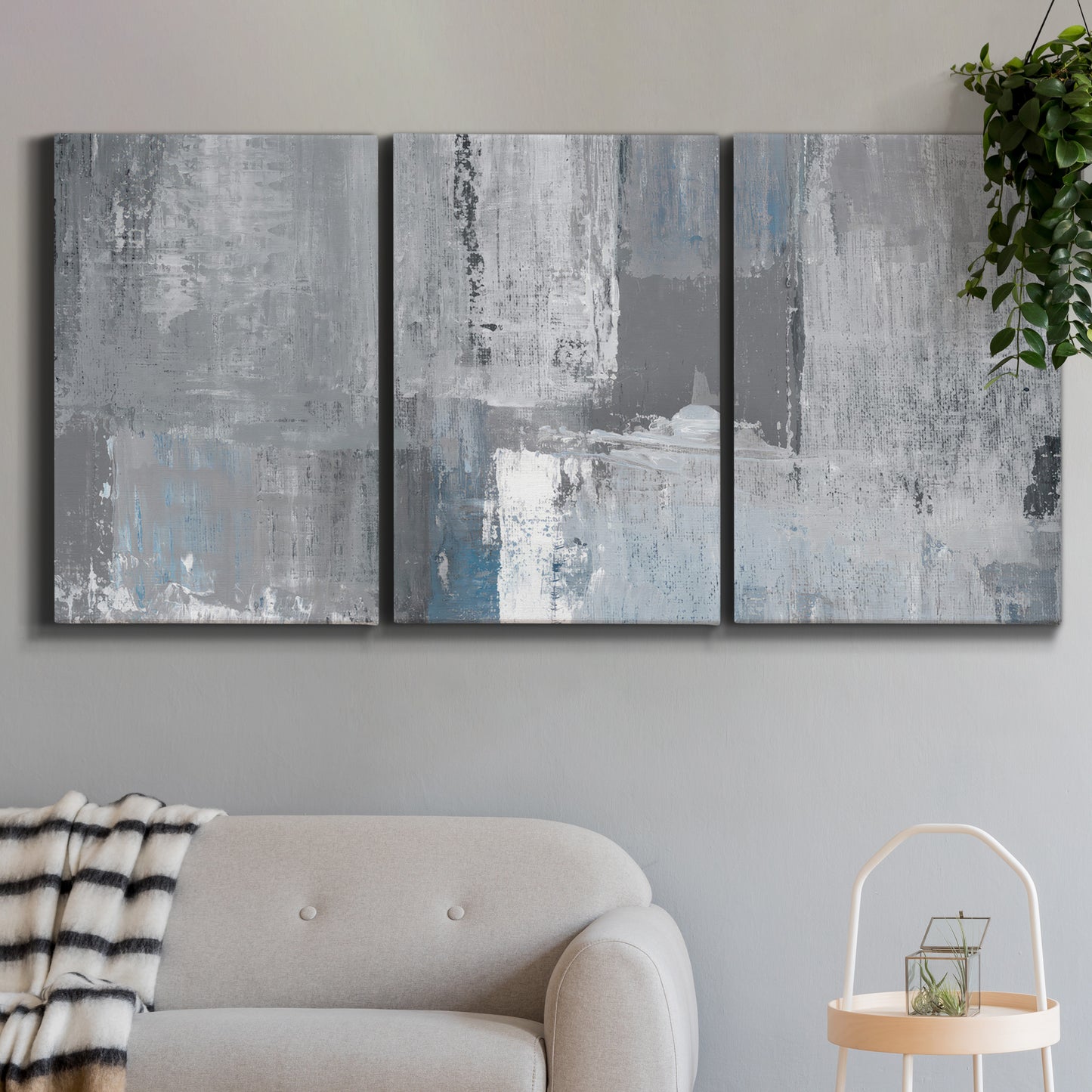 Three-panel canvas wall art featuring cool toned industrial abstract blues, displayed in a modern living room above a sofa.