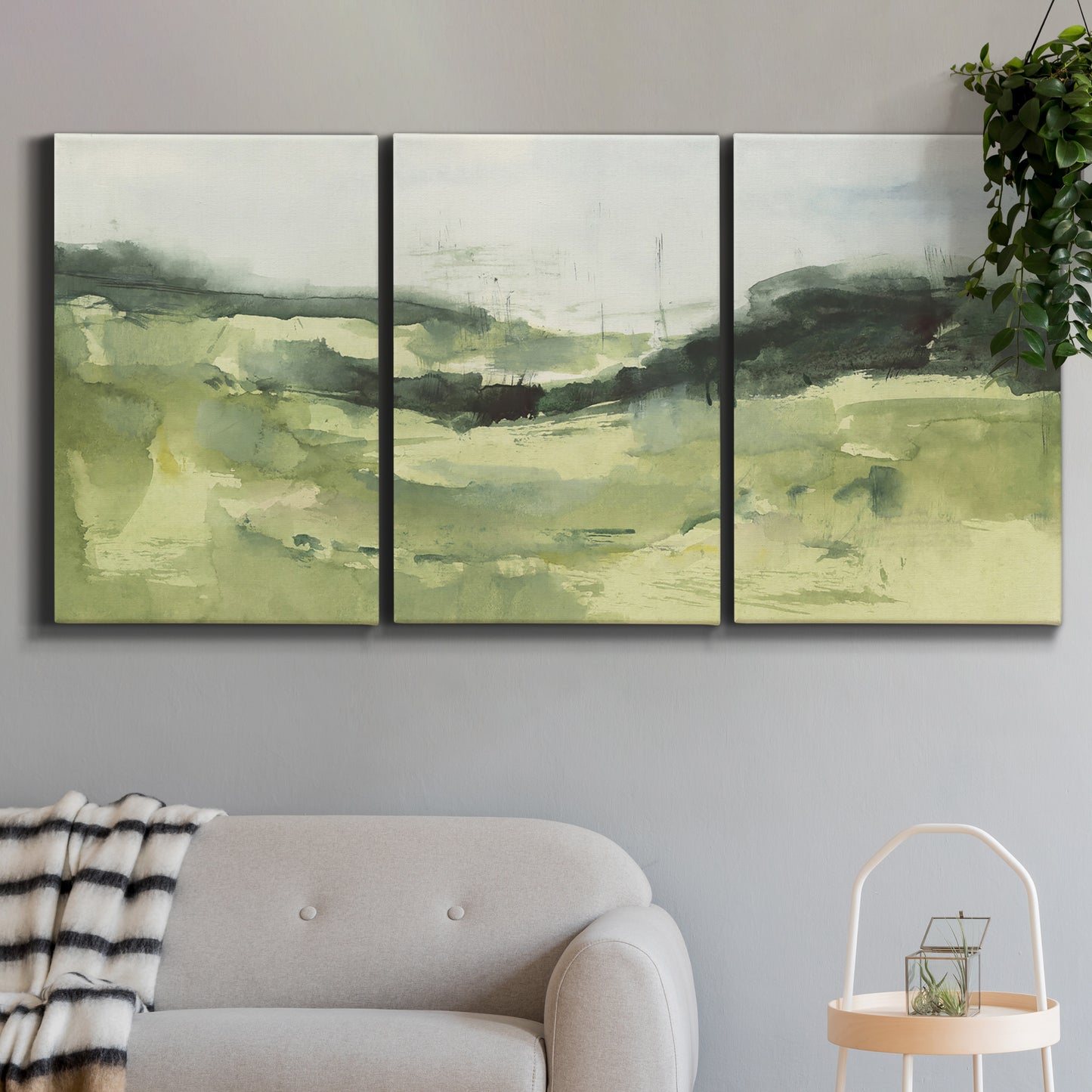 Three-panel canvas wall art featuring rolling hillside countryside landscape, displayed in a modern living room above a sofa.