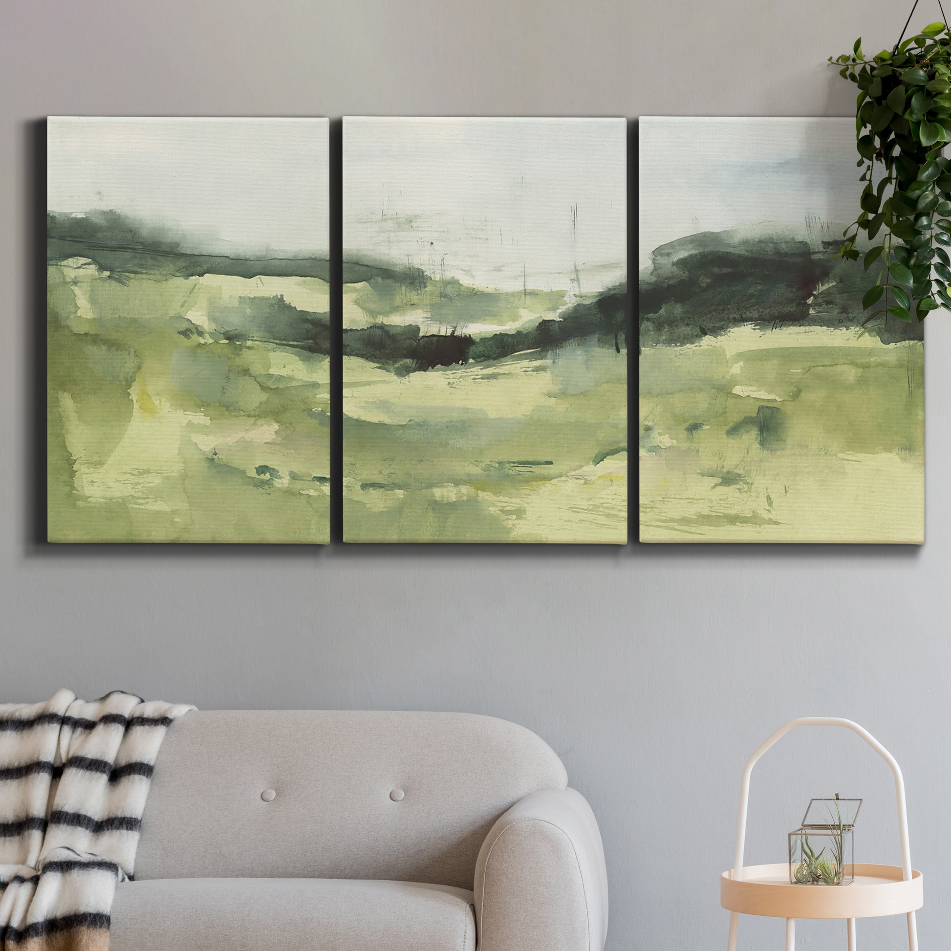 Three-panel canvas wall art featuring rolling hillside countryside landscape, displayed in a modern living room above a sofa.