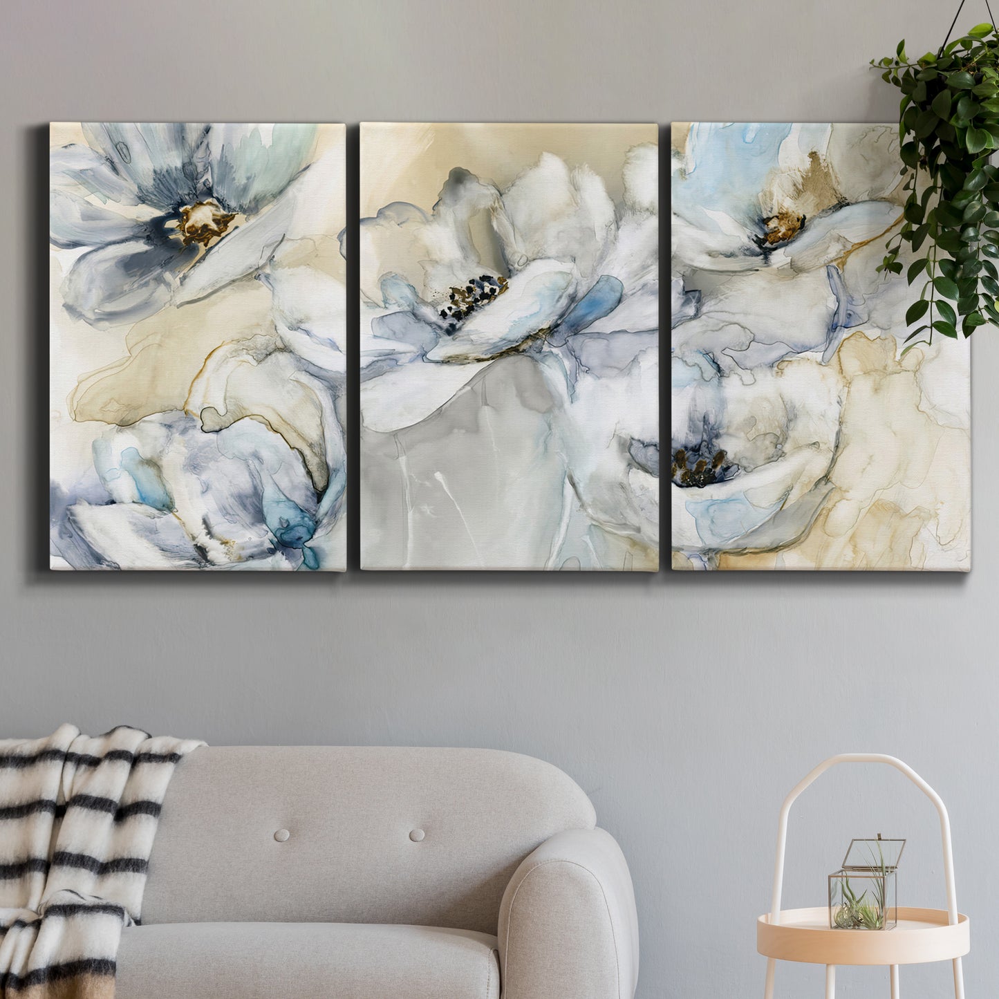 Three-panel canvas wall art featuring delicate watercolor floral blooms, displayed in a modern living room above a sofa.