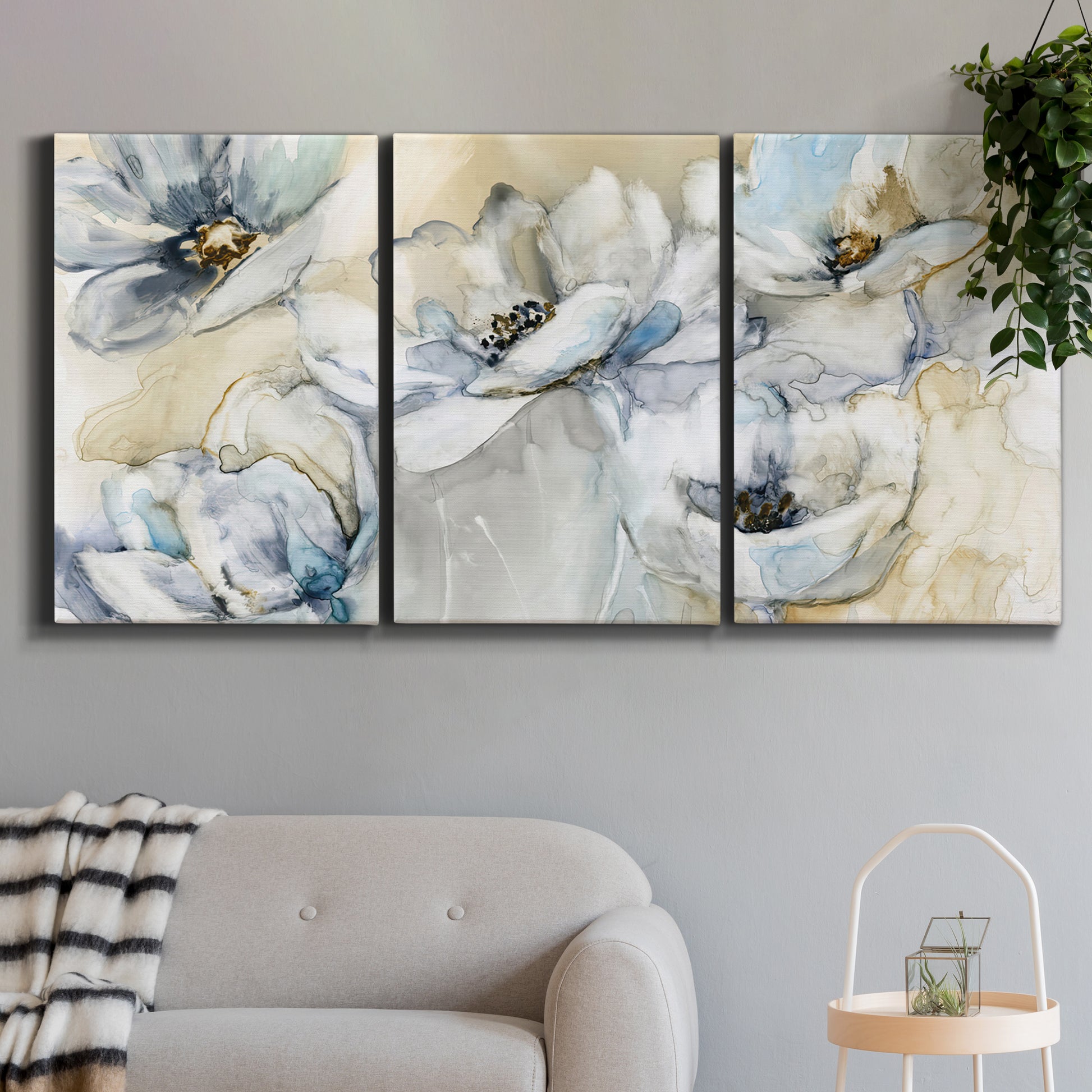 Three-panel canvas wall art featuring delicate watercolor floral blooms, displayed in a modern living room above a sofa.