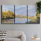 Three-panel canvas wall art featuring river flowing past village, displayed in a modern living room above a sofa.