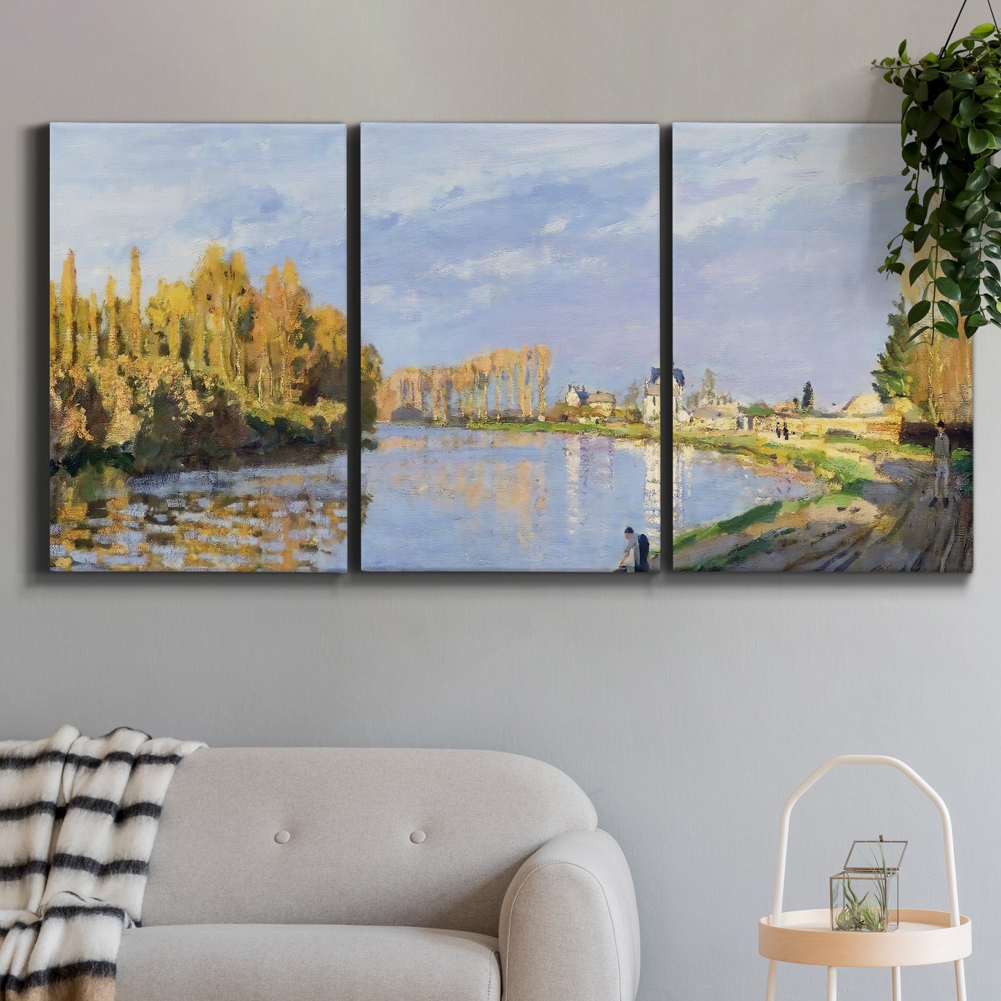 Three-panel canvas wall art featuring river flowing past village, displayed in a modern living room above a sofa.