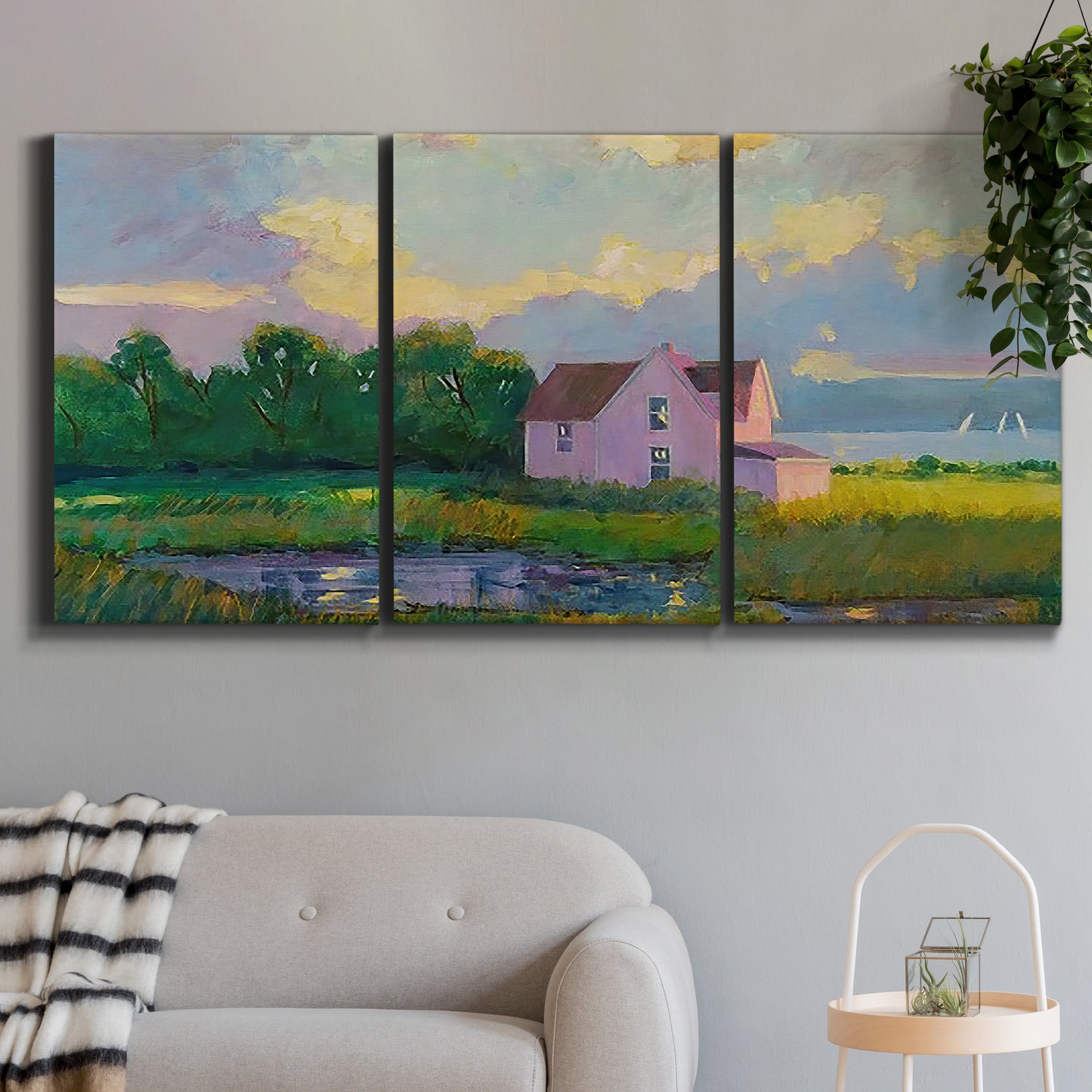Three-panel canvas wall art featuring farmhouse near coastline landscape, displayed in a modern living room above a sofa.