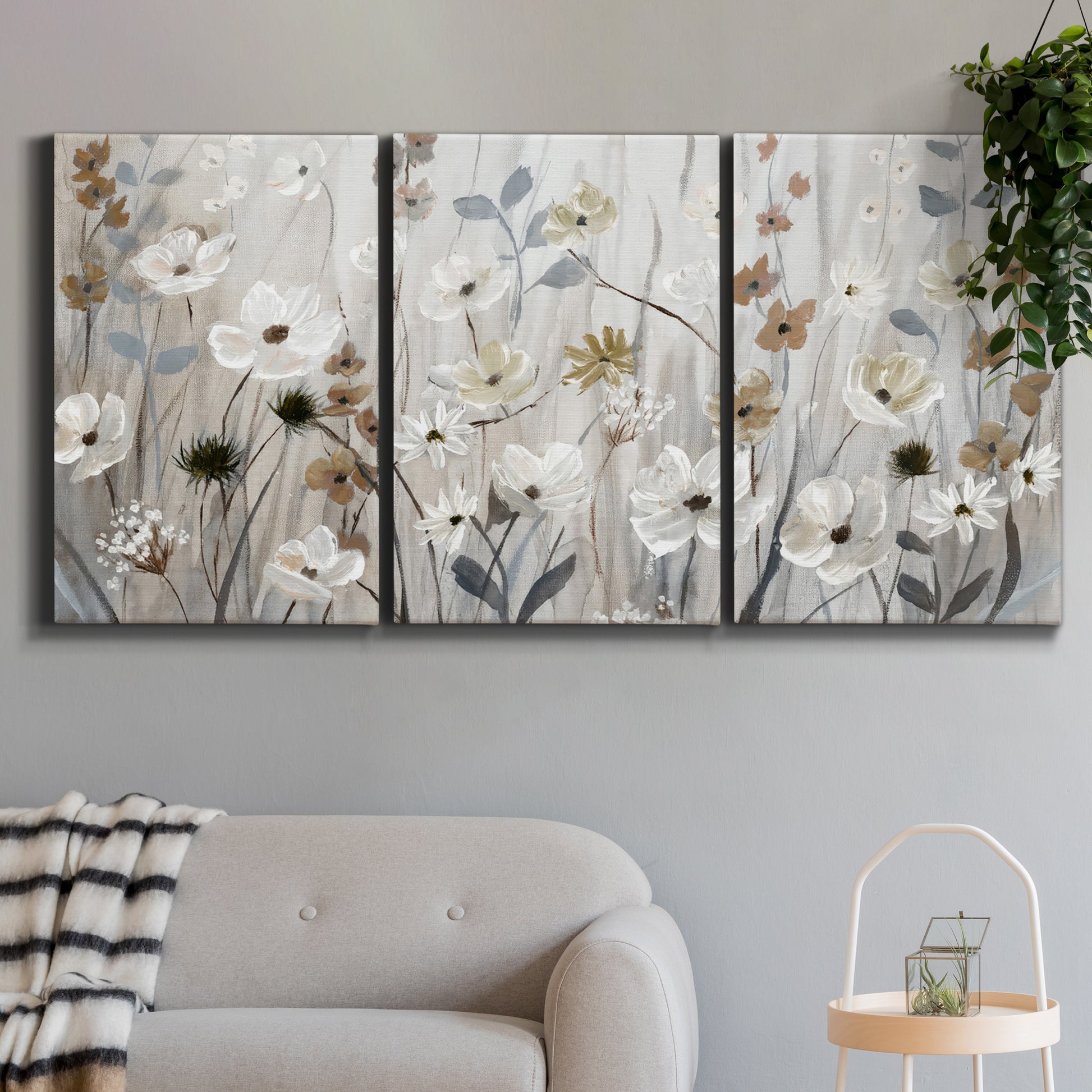 Three-panel canvas wall art featuring misty wildflower meadow landscape, displayed in a modern living room above a sofa.