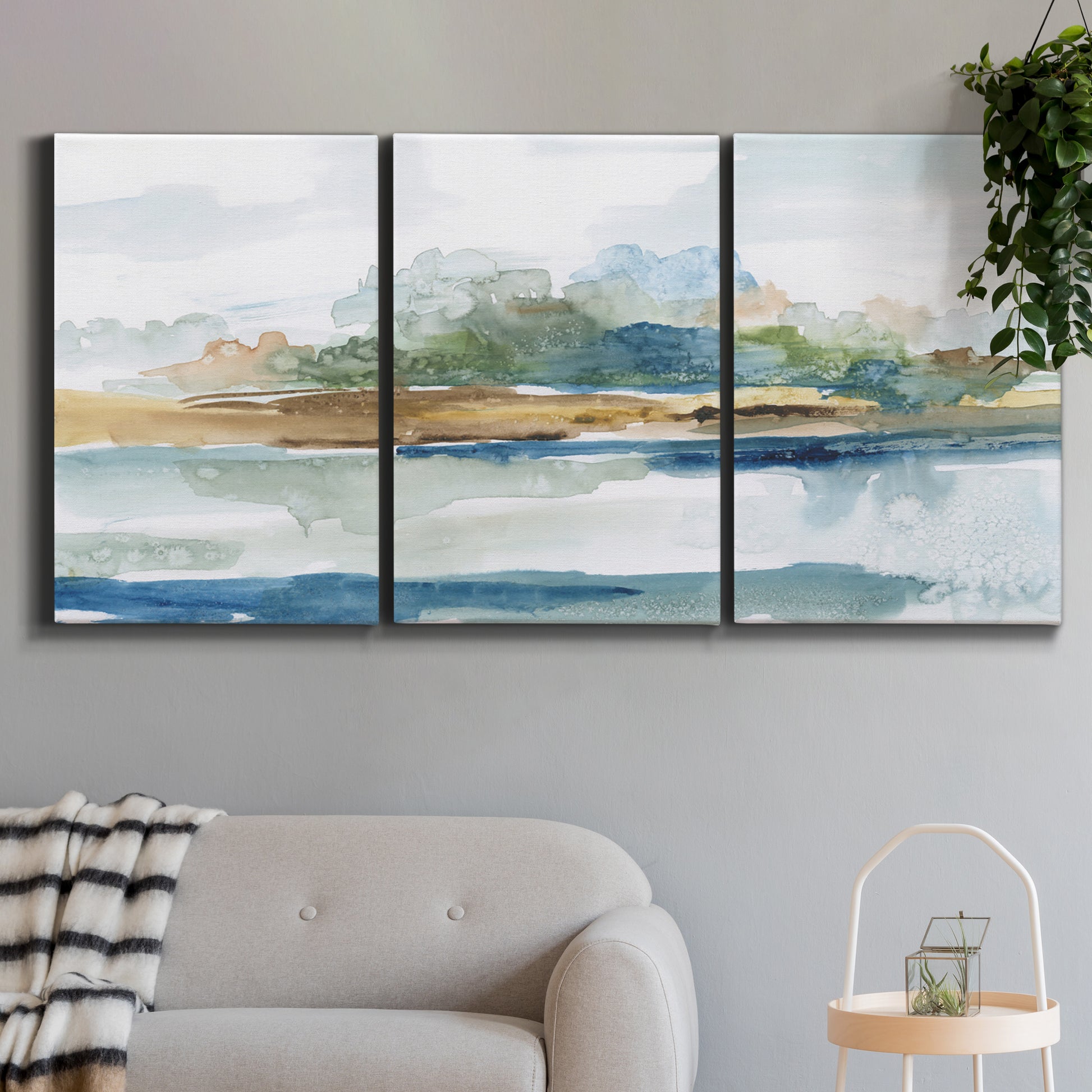 Three-panel canvas wall art featuring flowing blue abstract watercolor, displayed in a modern living room above a sofa.