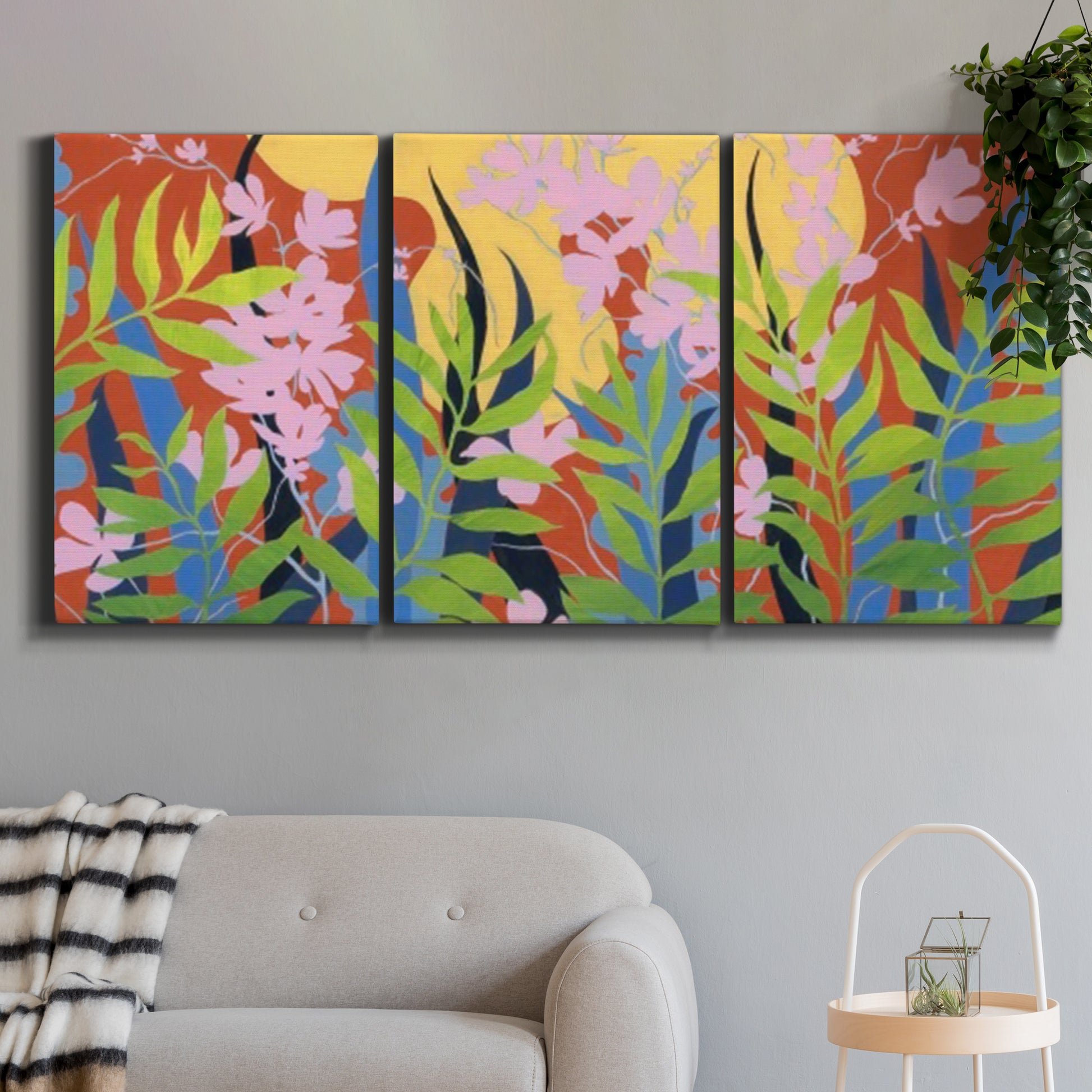 Three-panel canvas wall art featuring bold colorful floral abstraction, displayed in a modern living room above a sofa.