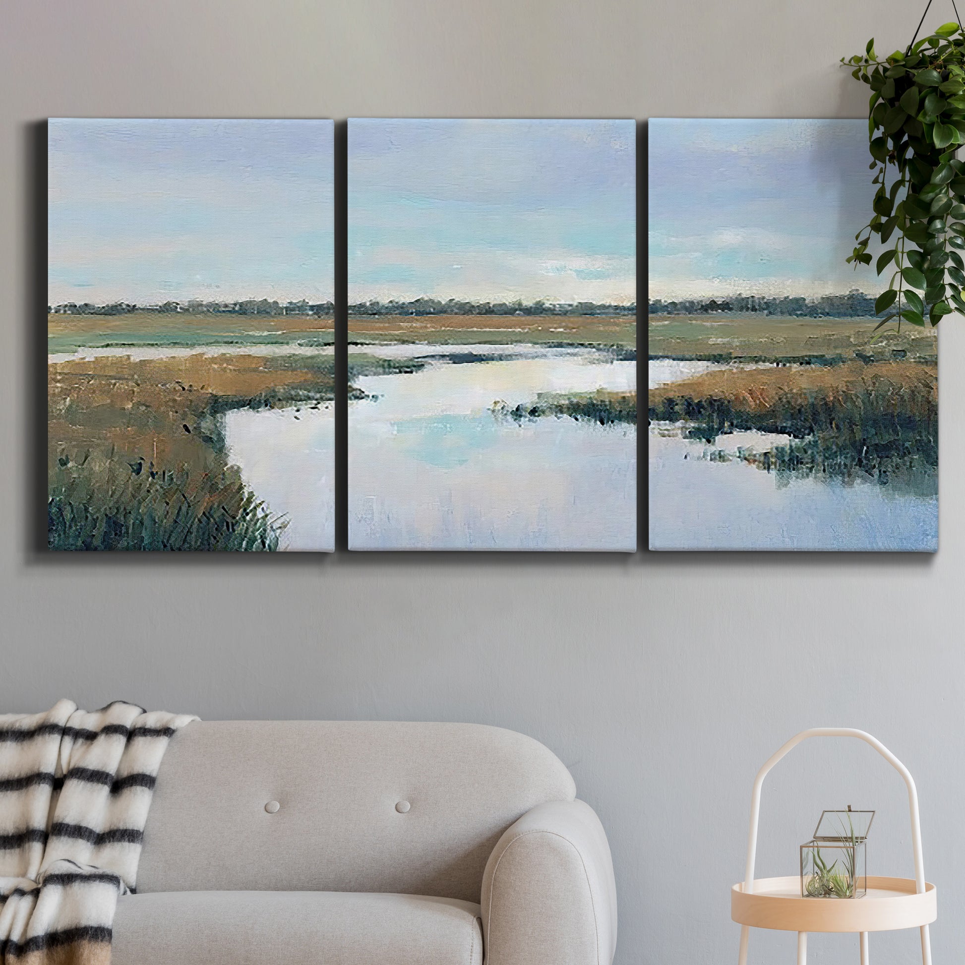 Three-panel canvas wall art featuring coastal plain meeting open water, displayed in a modern living room above a sofa.