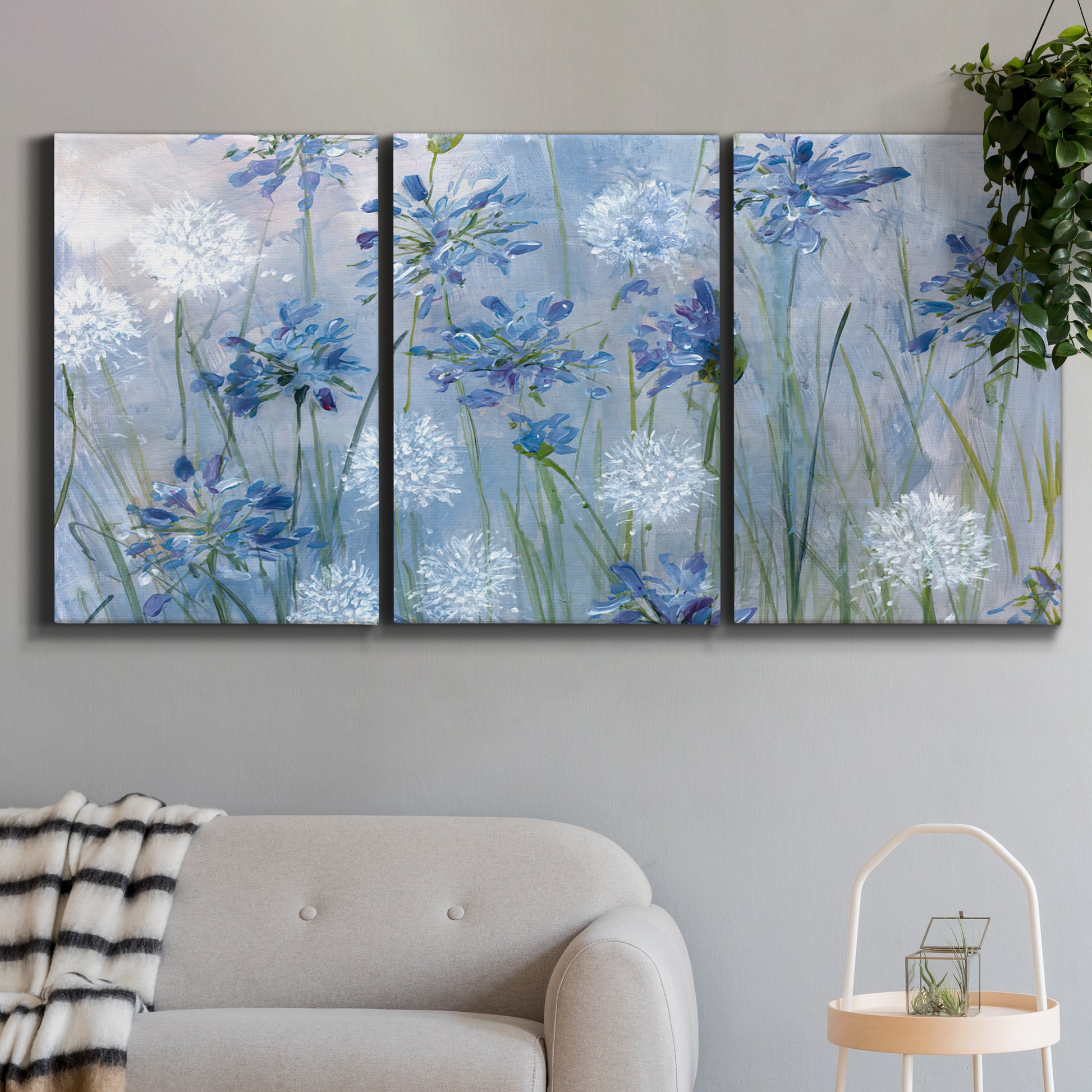 Three-panel canvas wall art featuring delicate watercolor floral blooms, displayed in a modern living room above a sofa.