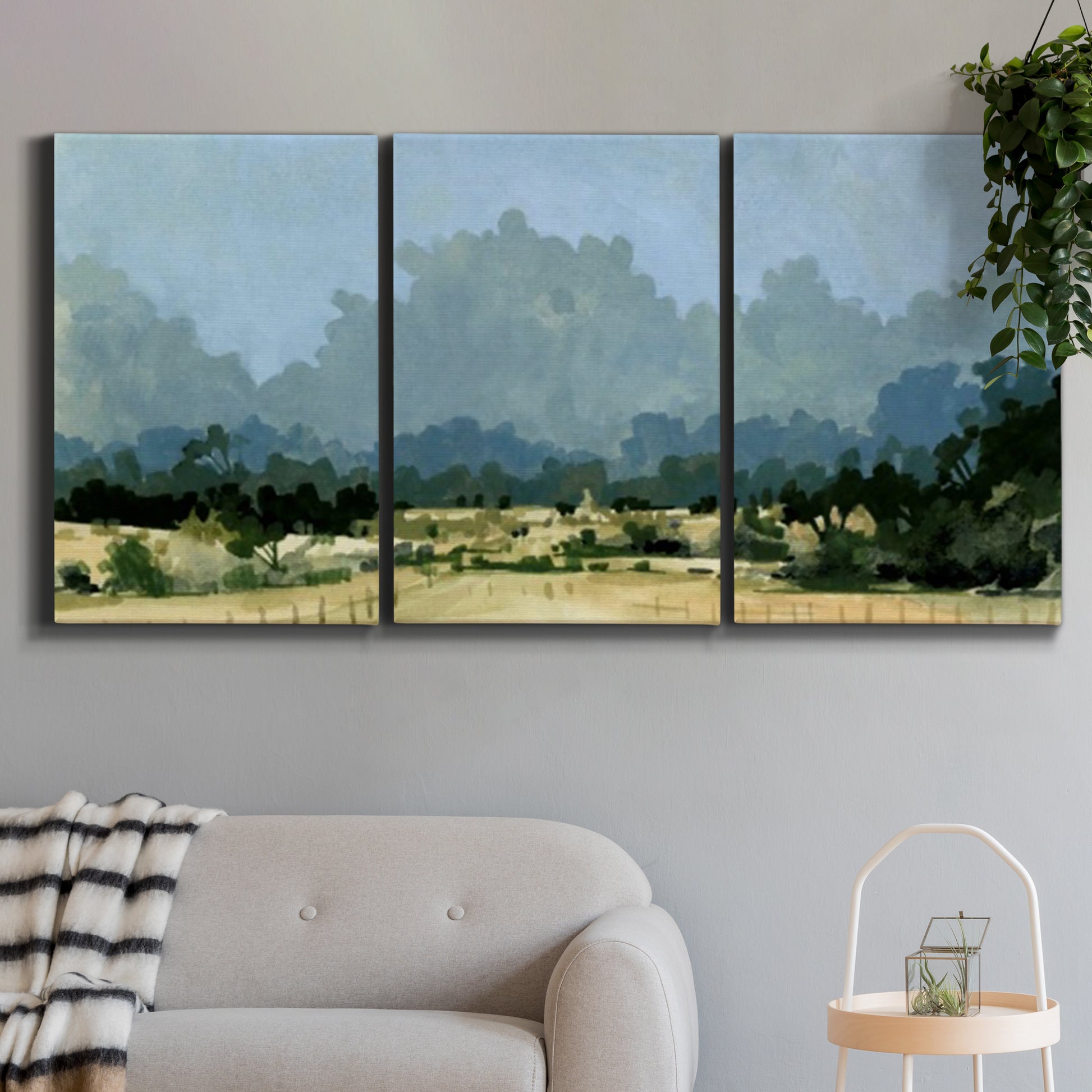 Three-panel canvas wall art featuring rural farmland landscape in watercolor, displayed in a modern living room above a sofa.