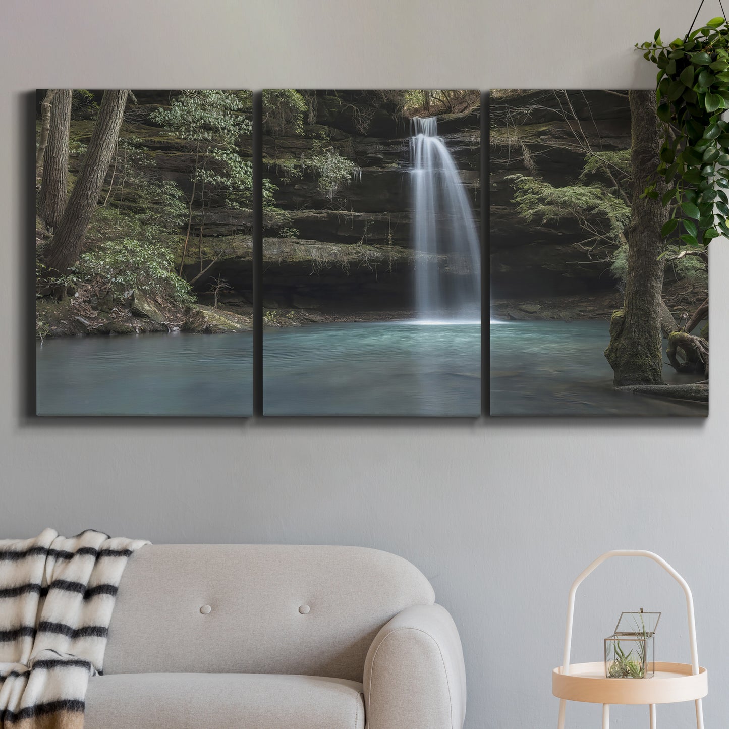 Three-panel canvas wall art featuring waterfall cascading through forest, displayed in a modern living room above a sofa.