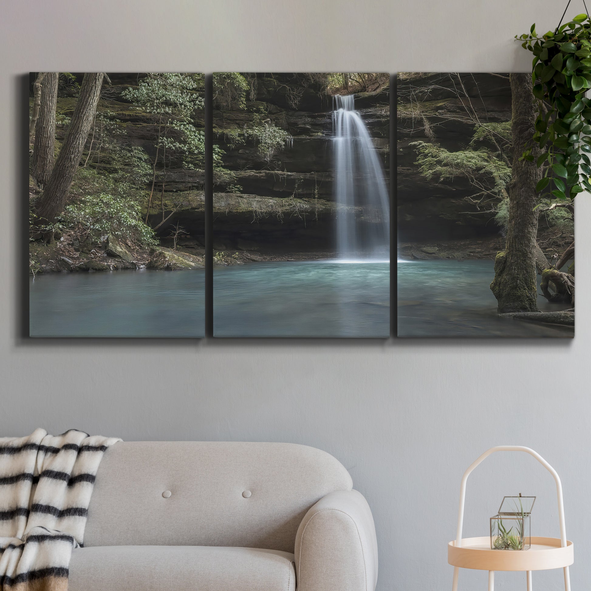 Three-panel canvas wall art featuring waterfall cascading through forest, displayed in a modern living room above a sofa.