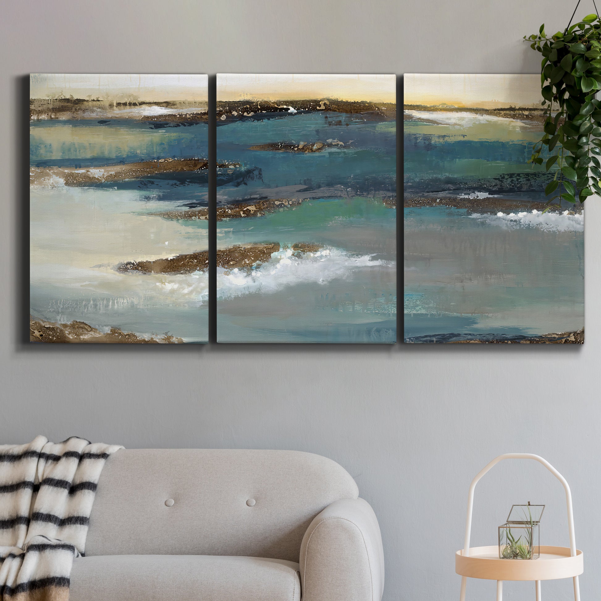 Three-panel canvas wall art featuring rocky coastal bluff above sea, displayed in a modern living room above a sofa.