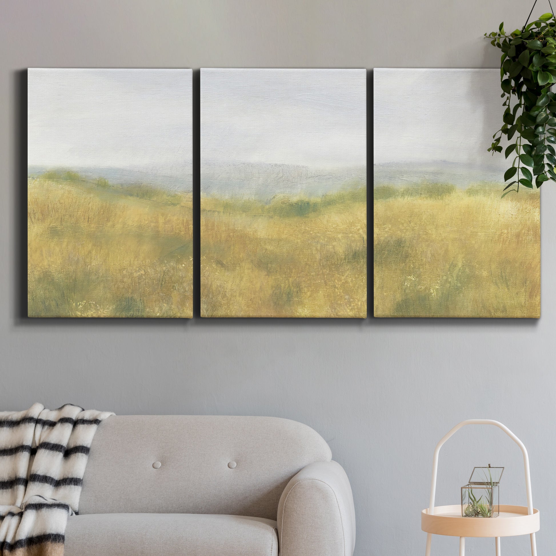 Three-panel canvas wall art featuring pastoral wheat field landscape, displayed in a modern living room above a sofa.