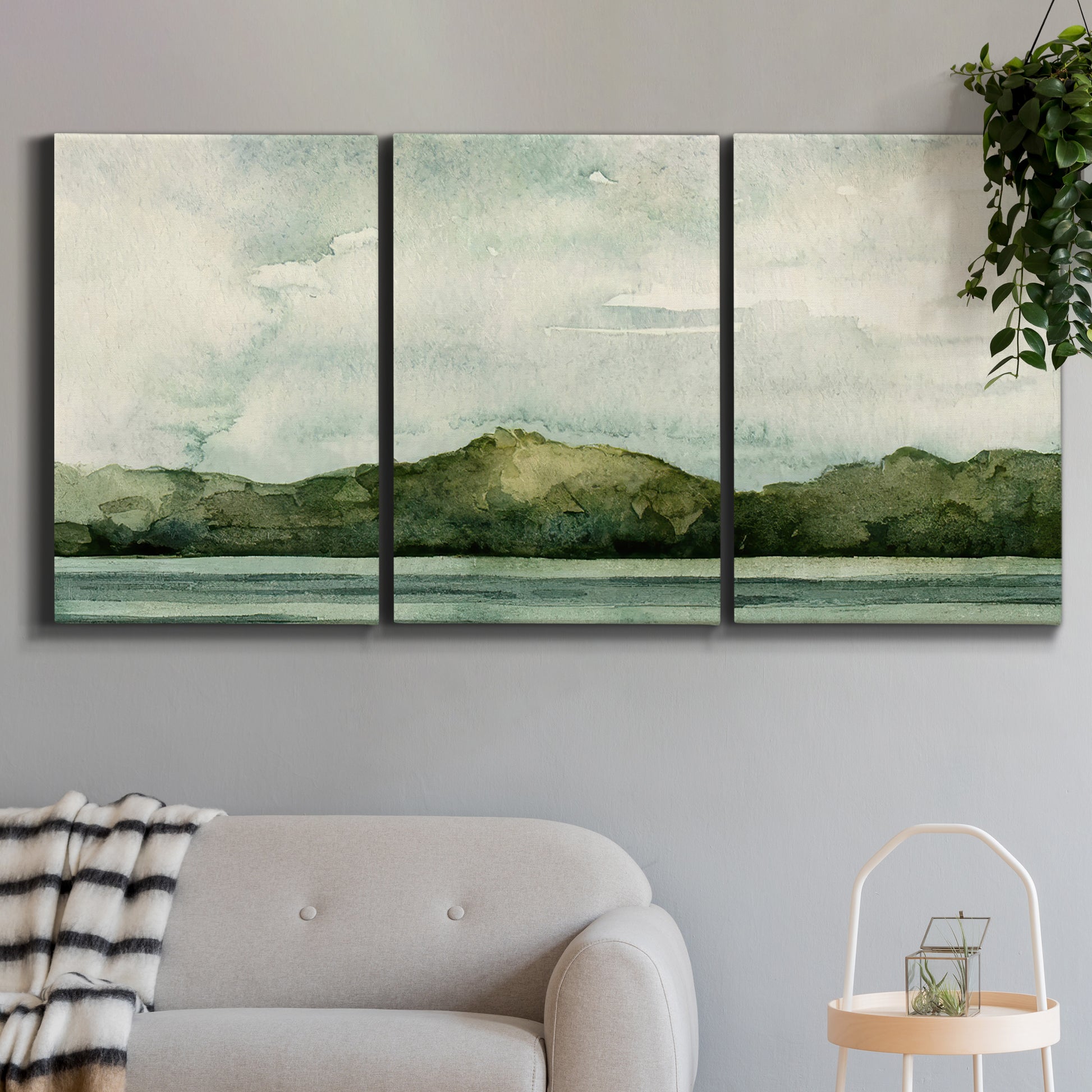 Three-panel canvas wall art featuring riverbank watercolor landscape, displayed in a modern living room above a sofa.