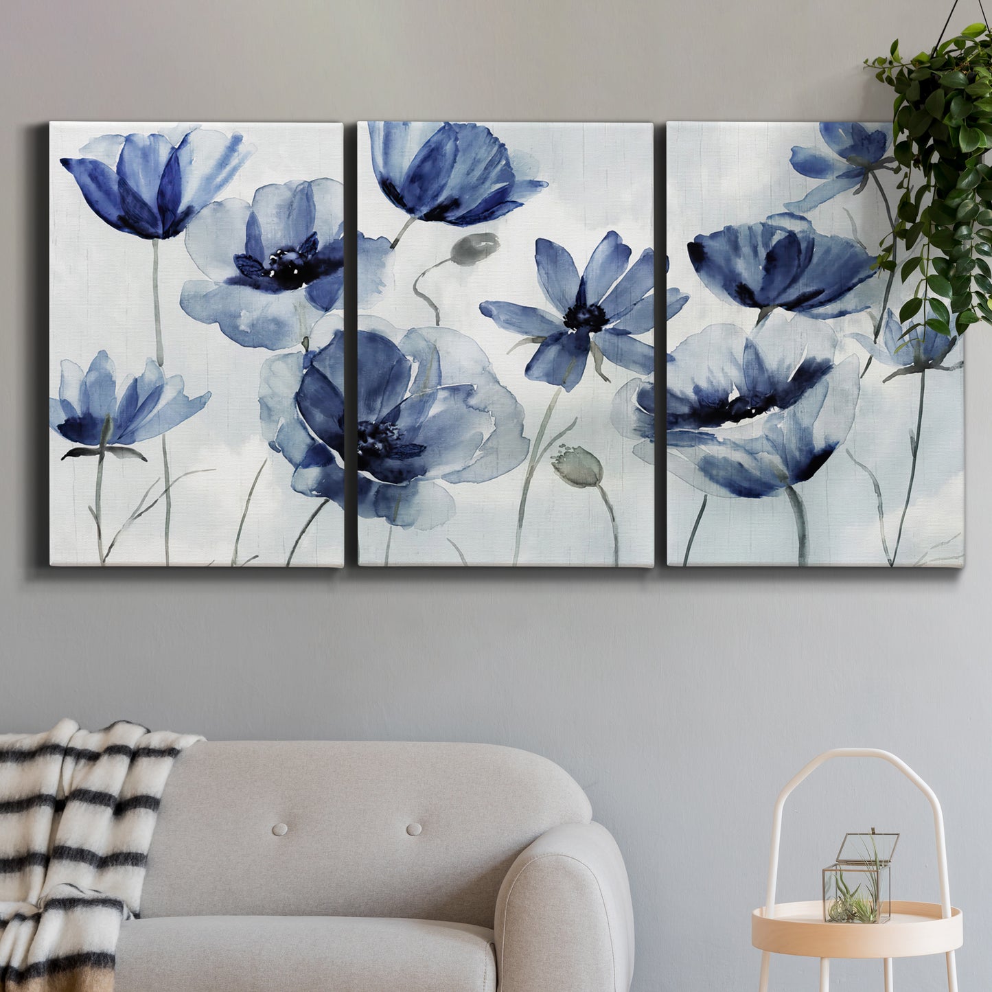 Three-panel canvas wall art featuring indigo floral blossoms awakening, displayed in a modern living room above a sofa.