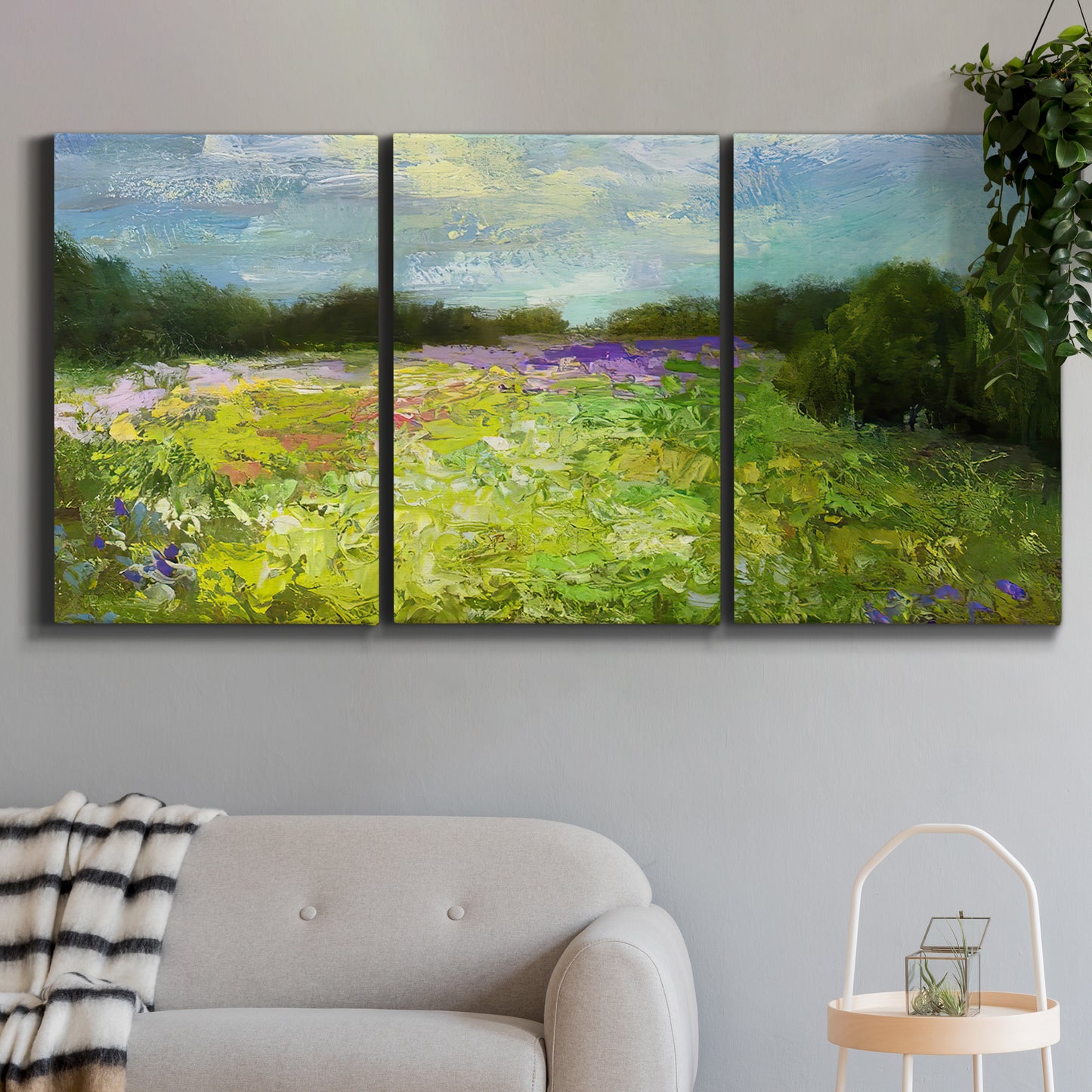 Three-panel canvas wall art featuring pastoral field with wildflowers, displayed in a modern living room above a sofa.