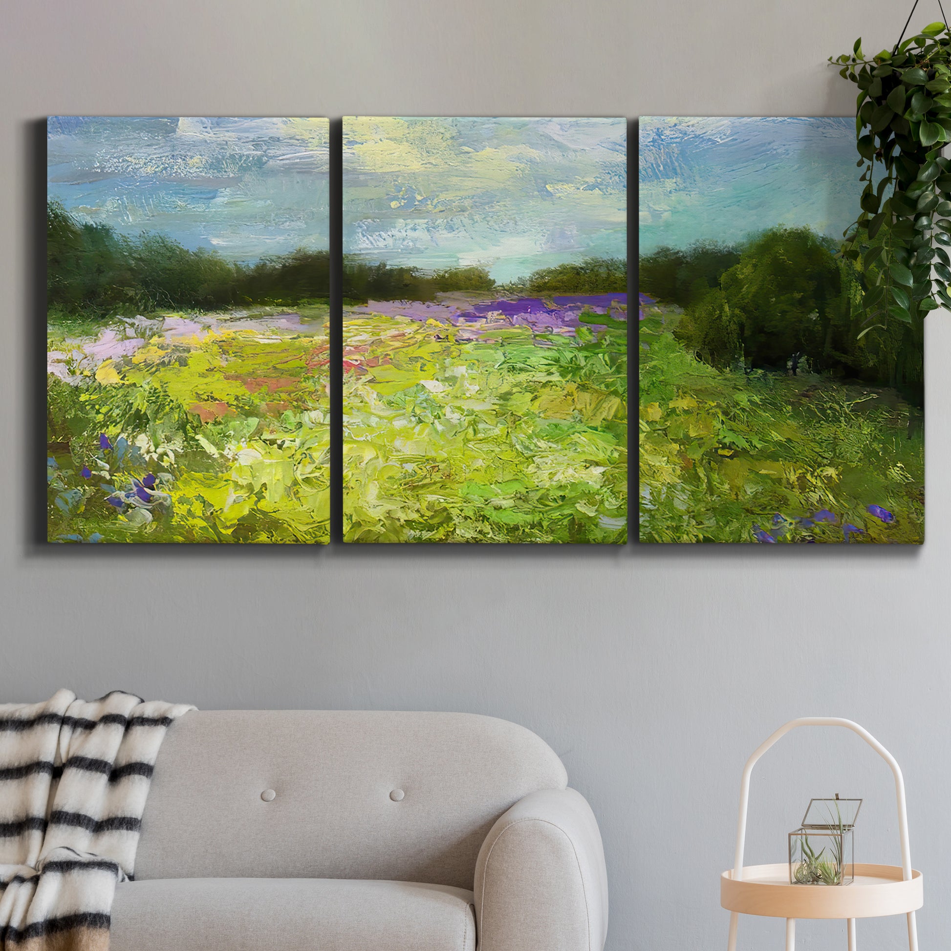 Three-panel canvas wall art featuring pastoral field with wildflowers, displayed in a modern living room above a sofa.