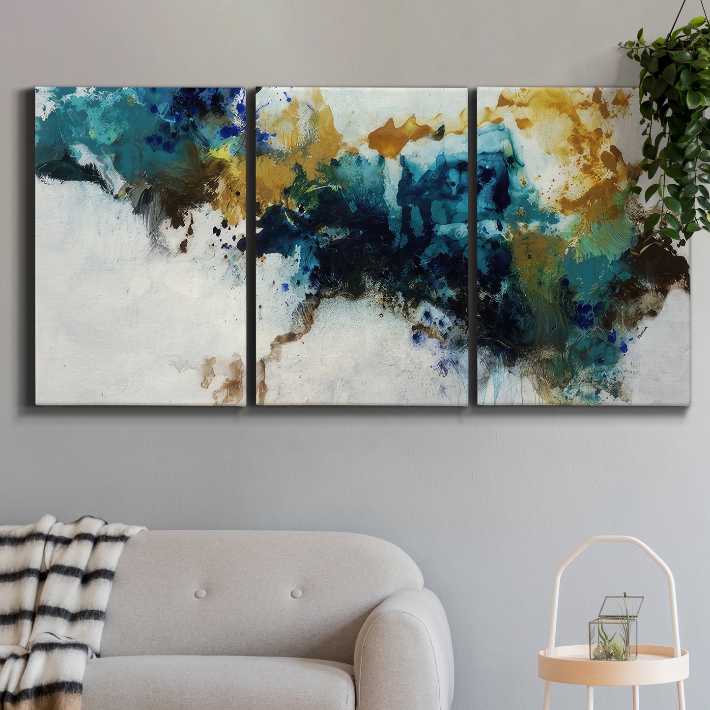 Three-panel canvas wall art featuring teal abstract paint splatter, displayed in a modern living room above a sofa.