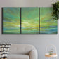 Three-panel canvas wall art featuring coastal shoreline under open sky, displayed in a modern living room above a sofa.