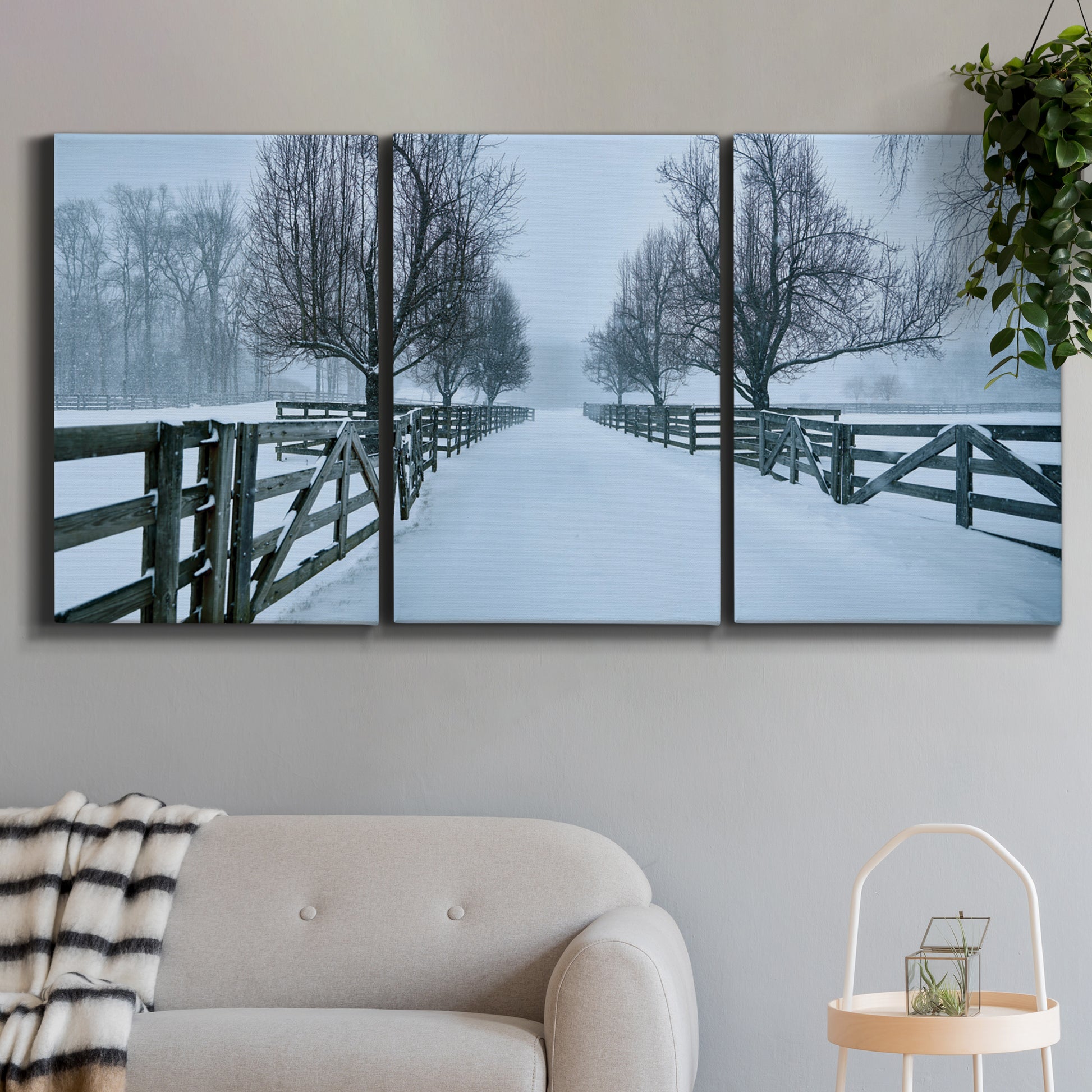 Three-panel canvas wall art featuring snow covered rural road photograph, displayed in a modern living room above a sofa.