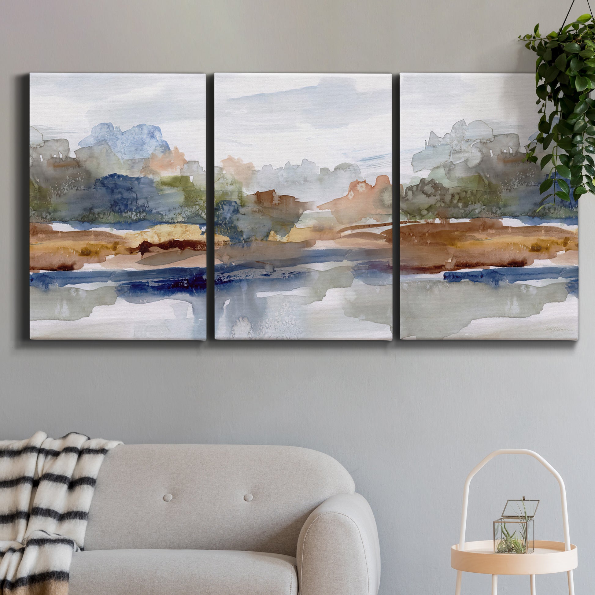 Three-panel canvas wall art featuring layered abstract mountain forms, displayed in a modern living room above a sofa.