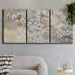 Three-panel canvas wall art featuring early spring blossoms in soft tones, displayed in a modern living room above a sofa.