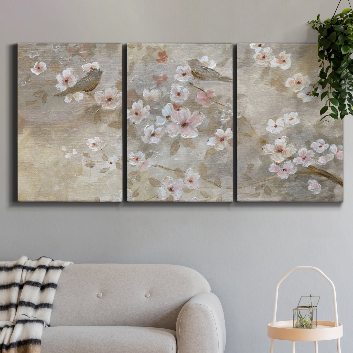 Three-panel canvas wall art featuring early spring blossoms in soft tones, displayed in a modern living room above a sofa.