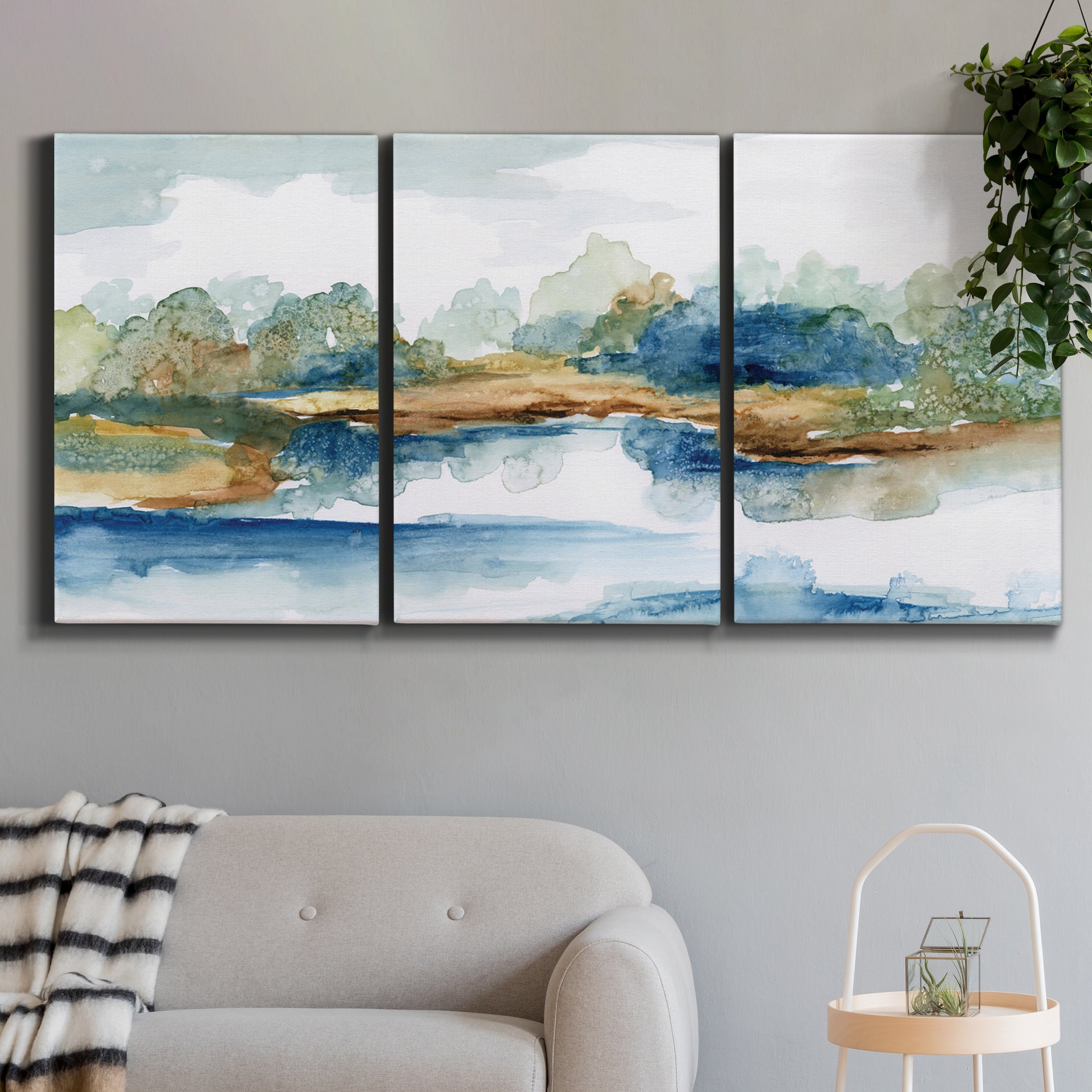 Three-panel canvas wall art featuring abstract blue watercolor landscape, displayed in a modern living room above a sofa.