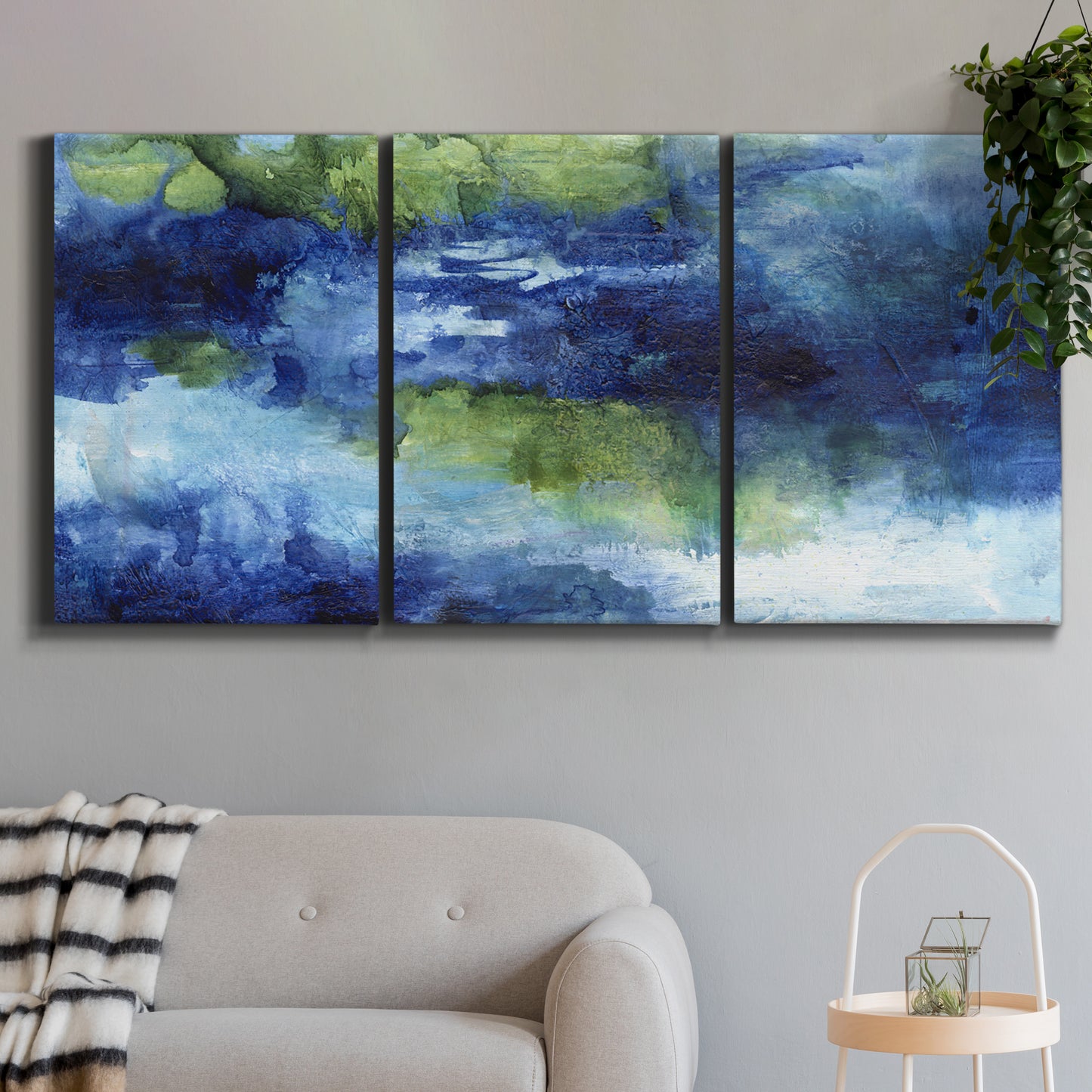 Three-panel canvas wall art featuring flowing blue abstract watercolor, displayed in a modern living room above a sofa.