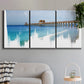 Three-panel canvas wall art featuring coastal pier extending over water, displayed in a modern living room above a sofa.