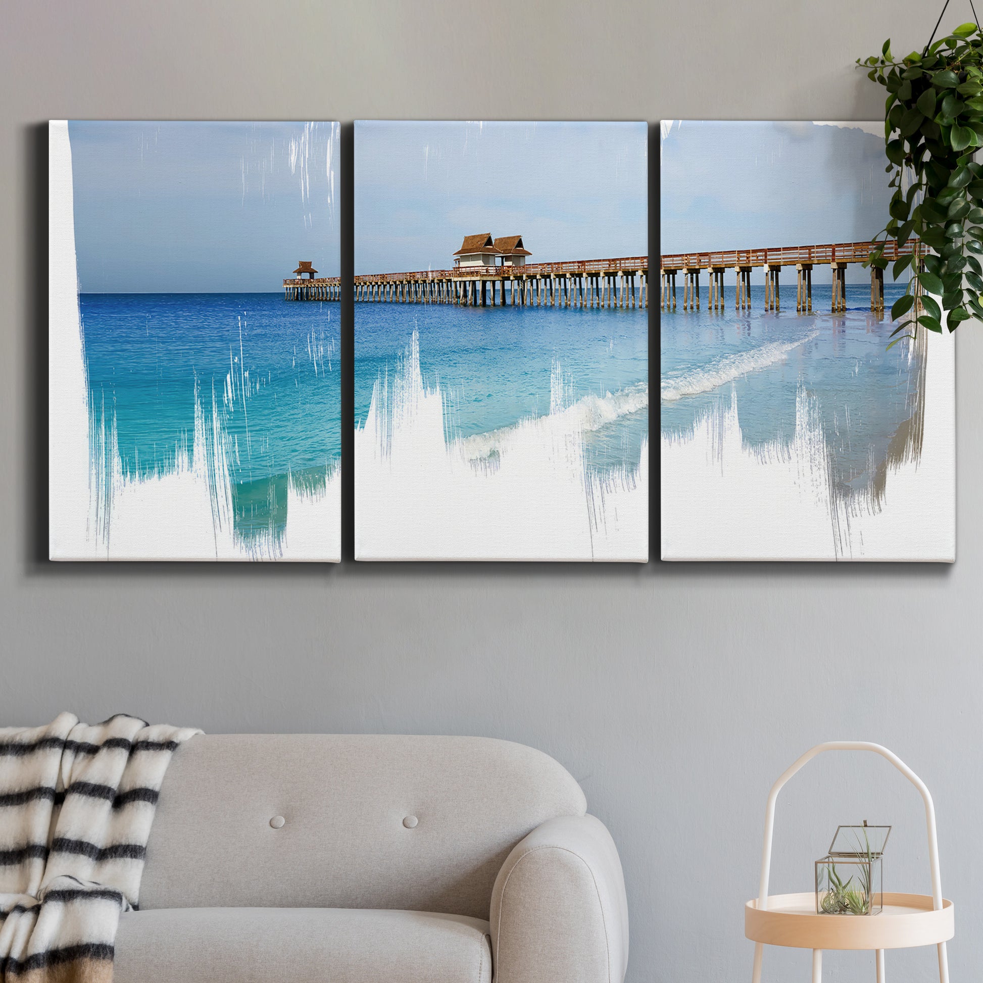 Three-panel canvas wall art featuring coastal pier extending over water, displayed in a modern living room above a sofa.