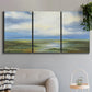 Three-panel canvas wall art featuring pastoral path leading into distance, displayed in a modern living room above a sofa.