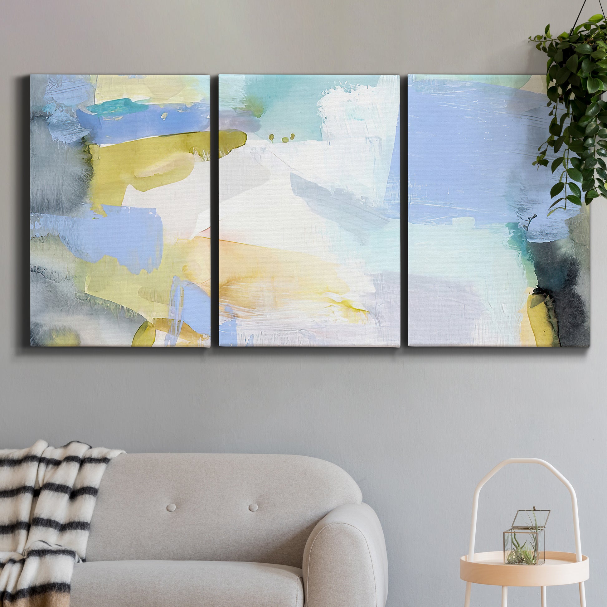 Three-panel canvas wall art featuring soft abstract spring watercolor tones, displayed in a modern living room above a sofa.