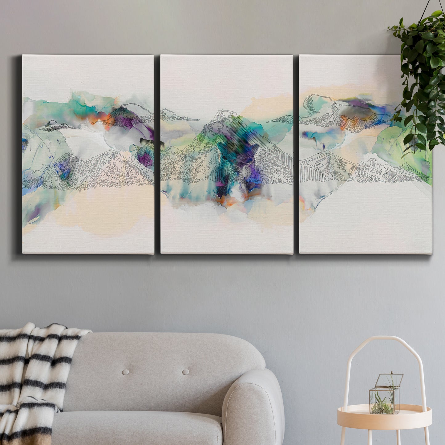 Three-panel canvas wall art featuring abstract mountain range watercolor, displayed in a modern living room above a sofa.