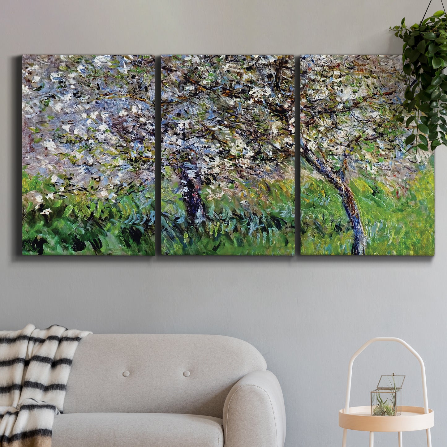 Three-panel canvas wall art featuring apple trees blooming beside water, displayed in a modern living room above a sofa.