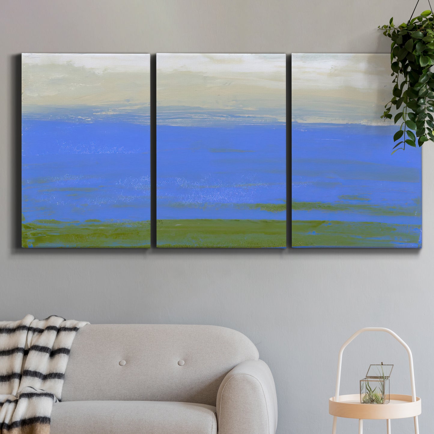 Three-panel canvas wall art featuring abstract coastal inlet landscape, displayed in a modern living room above a sofa.