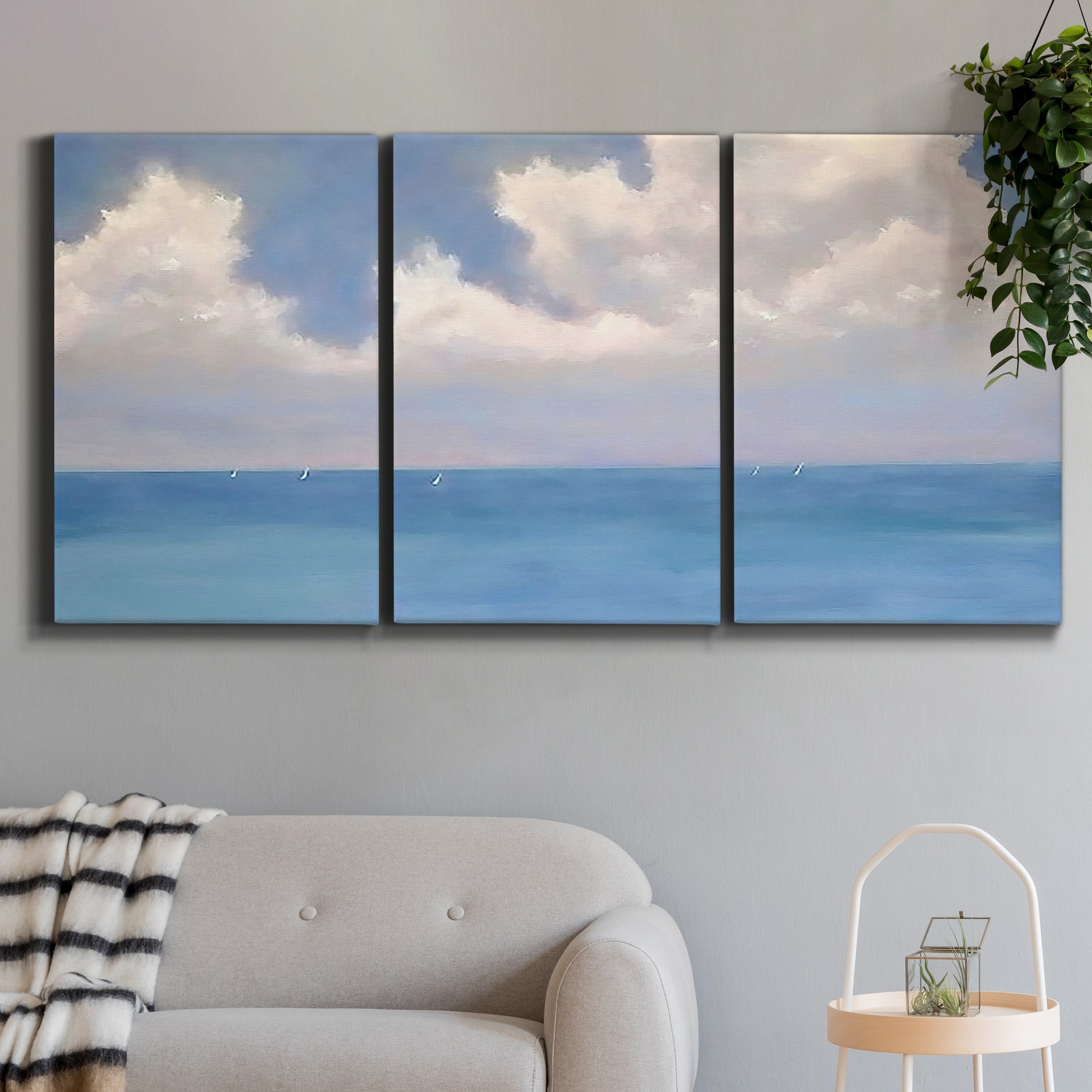 Three-panel canvas wall art featuring coastal shoreline with distant horizon, displayed in a modern living room above a sofa.