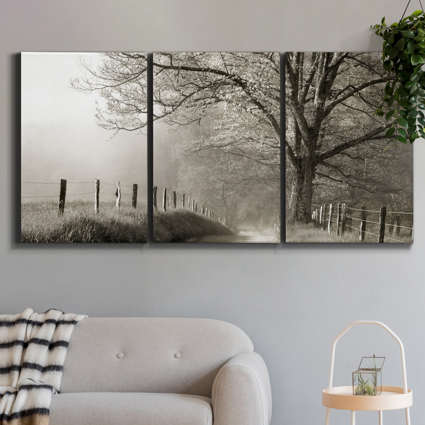 Three-panel canvas wall art featuring fenced rural path through countryside, displayed in a modern living room above a sofa.