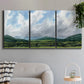 Three-panel canvas wall art featuring pastoral mountain landscape in blue, displayed in a modern living room above a sofa.