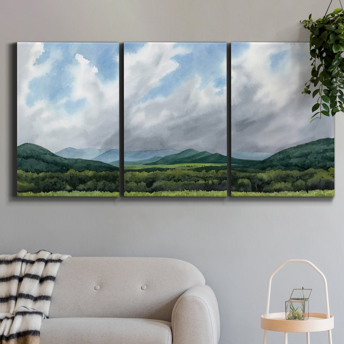 Three-panel canvas wall art featuring pastoral mountain landscape in blue, displayed in a modern living room above a sofa.
