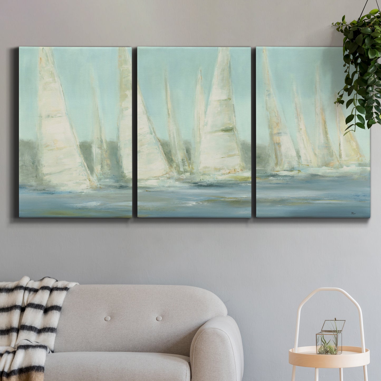 Three-panel canvas wall art featuring sailboats silhouetted at sunrise, displayed in a modern living room above a sofa.
