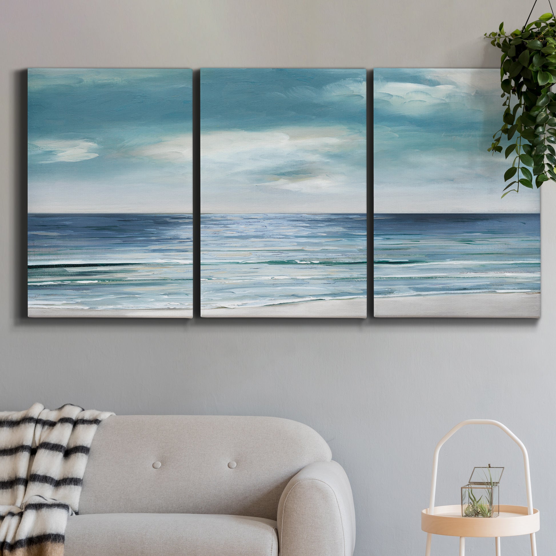 Three-panel canvas wall art featuring calm coastal shoreline, displayed in a modern living room above a sofa.