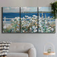 Three-panel canvas wall art featuring coastal garden overlooking bay, displayed in a modern living room above a sofa.