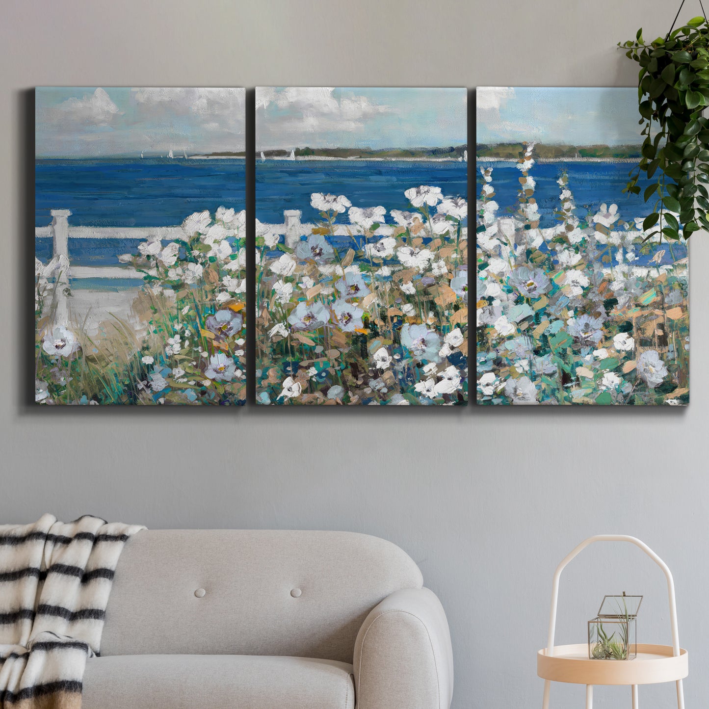 Three-panel canvas wall art featuring coastal garden overlooking bay, displayed in a modern living room above a sofa.