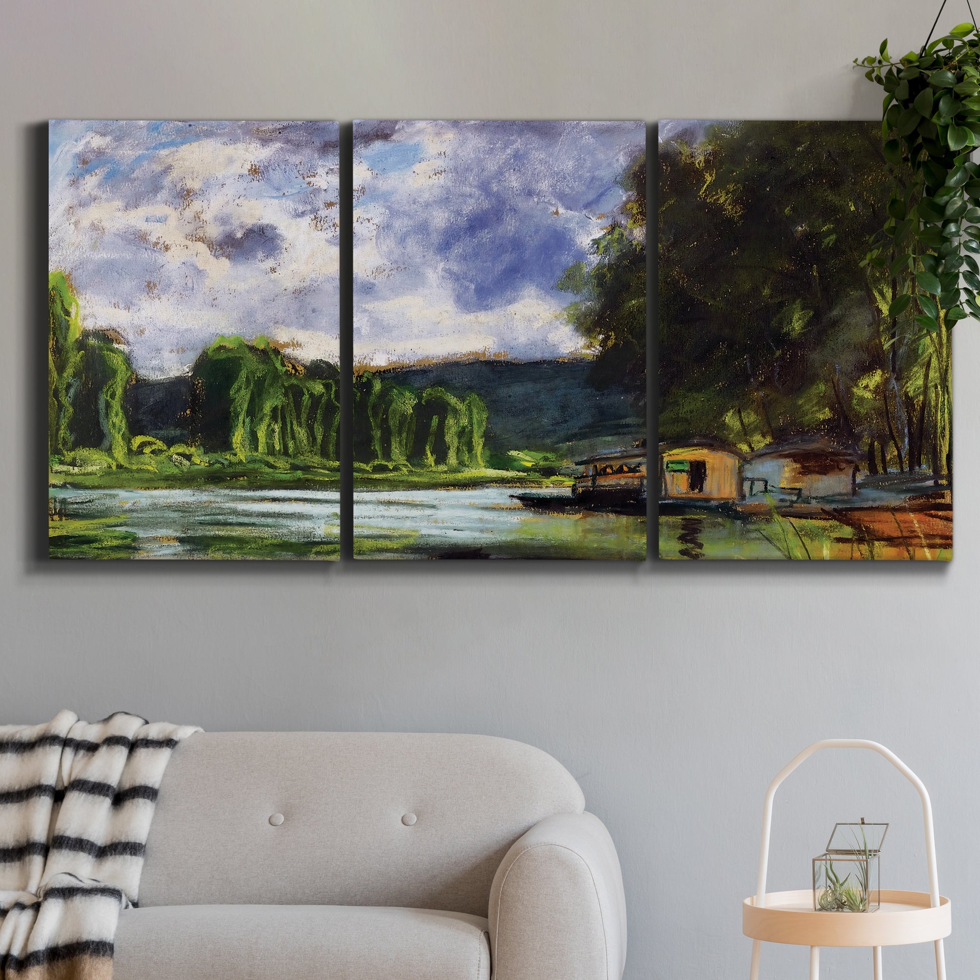 Three-panel canvas wall art featuring riverbank landscape near village, displayed in a modern living room above a sofa.